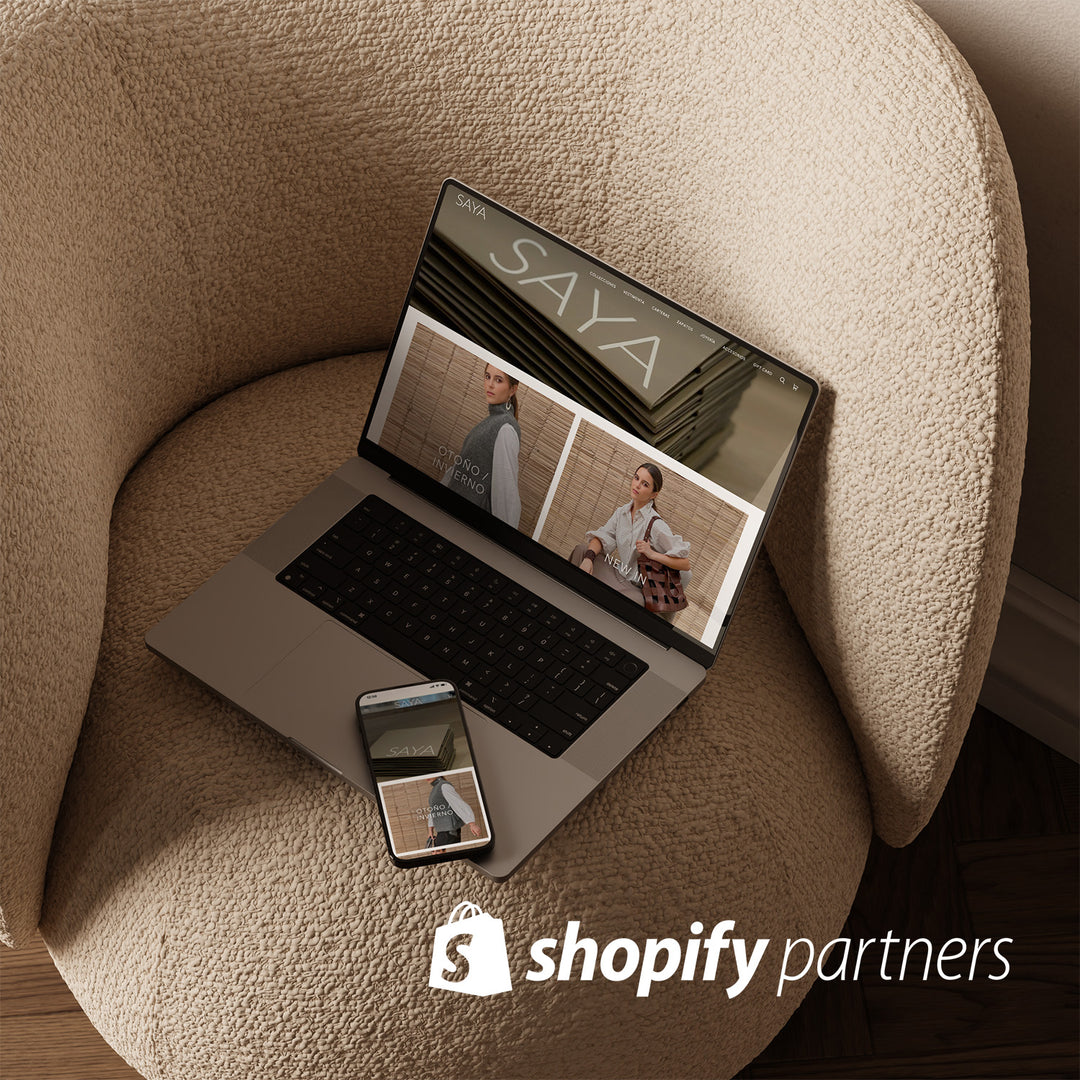 Una laptop abierta sobre un sillón y a su lado un iphone. En la pantalla de ambos se ve la página web de Saya.  Encima de la imagen está sobreimpreso el logo de Shopify Partners.