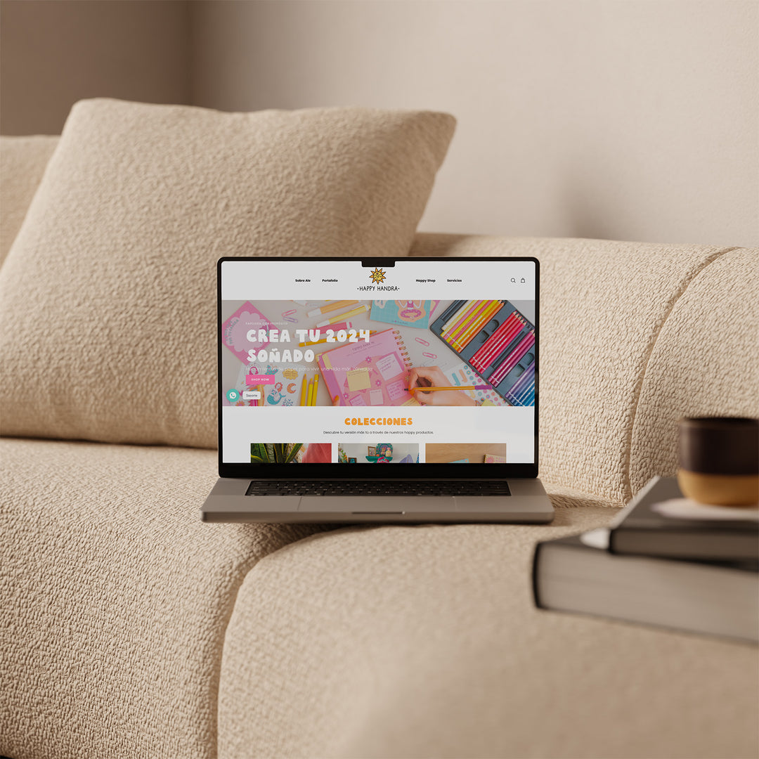 Una laptop abierta apoyada sobre un sillón. En su pantalla se ve el inicio de la página web de la artista Happy Handra.