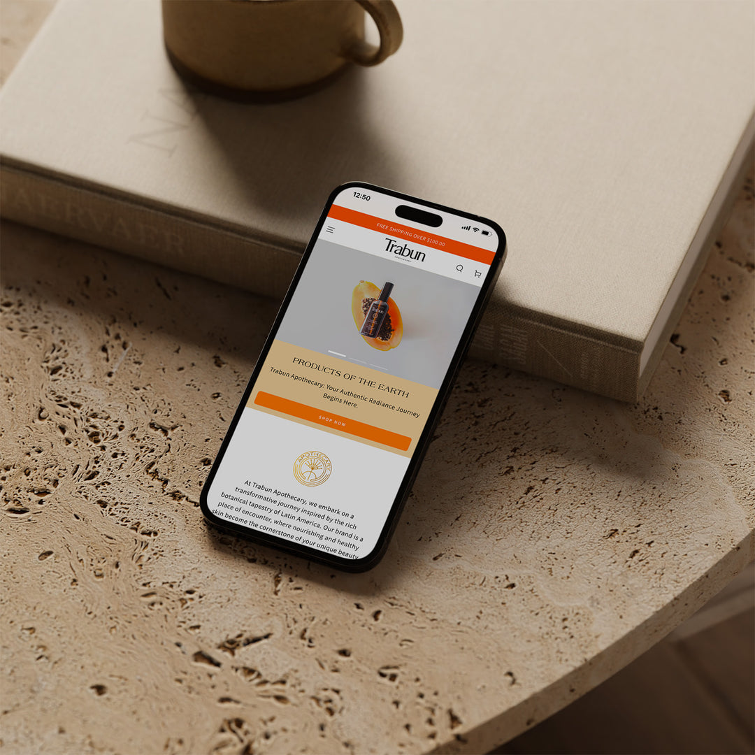 Un Iphone apoyado sobre una mesa. En su pantalla se encuentra el inicio de la página web de la marca Trabun.