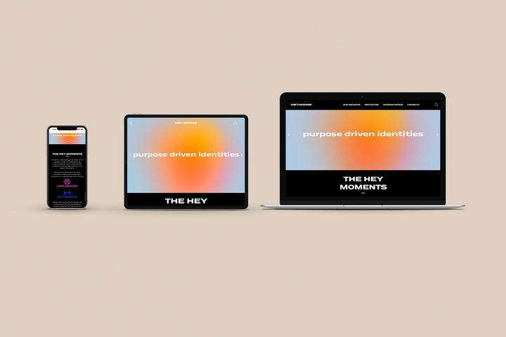 Un Iphone, un Ipad y una laptop mostrando cada uno el inicio de la página web de Hey Mome. Los tres dispositivos están uno al lado del otro sobre un fondo color entero beige. 