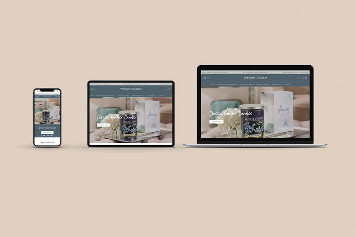 Un Iphone, un Ipad y una laptop mostrando cada uno el inicio de la página web de Yankee Candle. Los tres dispositivos están uno al lado del otro sobre un fondo color entero beige. 